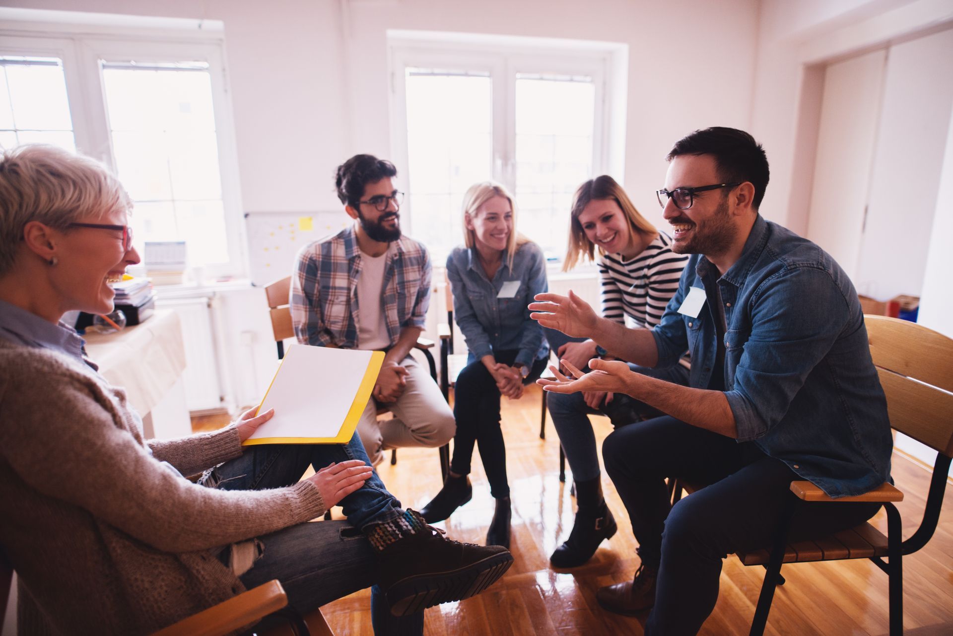 People seated in a circle, engaged in a discussion; a woman holds papers. People seated in a circle, engaged in a discussion; a woman holds papers.