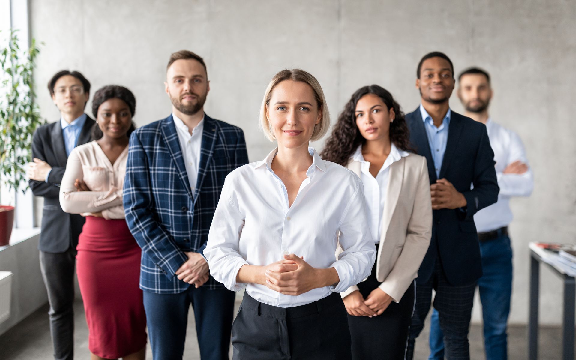 Group of professionals standing together indoors. The central woman smiles. Others have neutral expressions. Group of professionals standing together indoors. The central woman smiles. Others have neutral expressions.