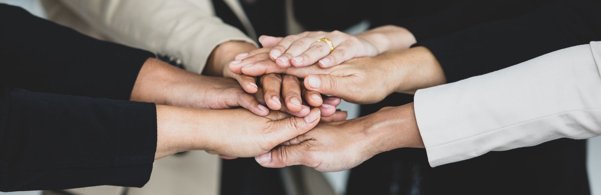Hands stacked on top of each other, in a sign of teamwork or solidarity, with sleeves of varying colors visible. Hands stacked on top of each other, in a sign of teamwork or solidarity, with sleeves of varying colors visible.