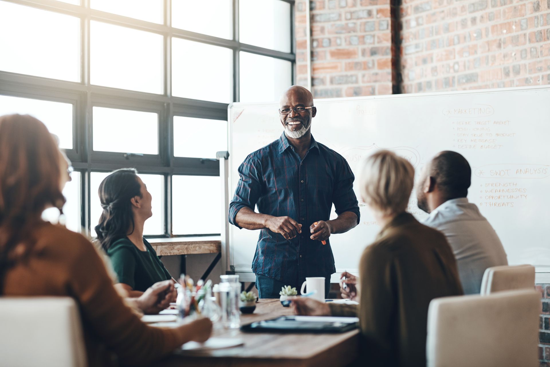 Man presenting in meeting to colleagues, whiteboard in background. Man presenting in meeting to colleagues, whiteboard in background.