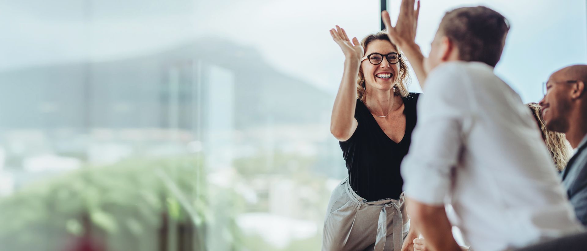 People giving high-fives in an office, celebrating a success. Focus is on a smiling woman.