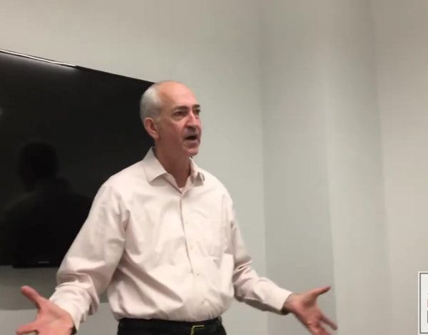 Man in a suit smiles, sitting near a window with a city view; interview setting.