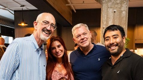 Man in a suit smiles, sitting near a window with a city view; interview setting.