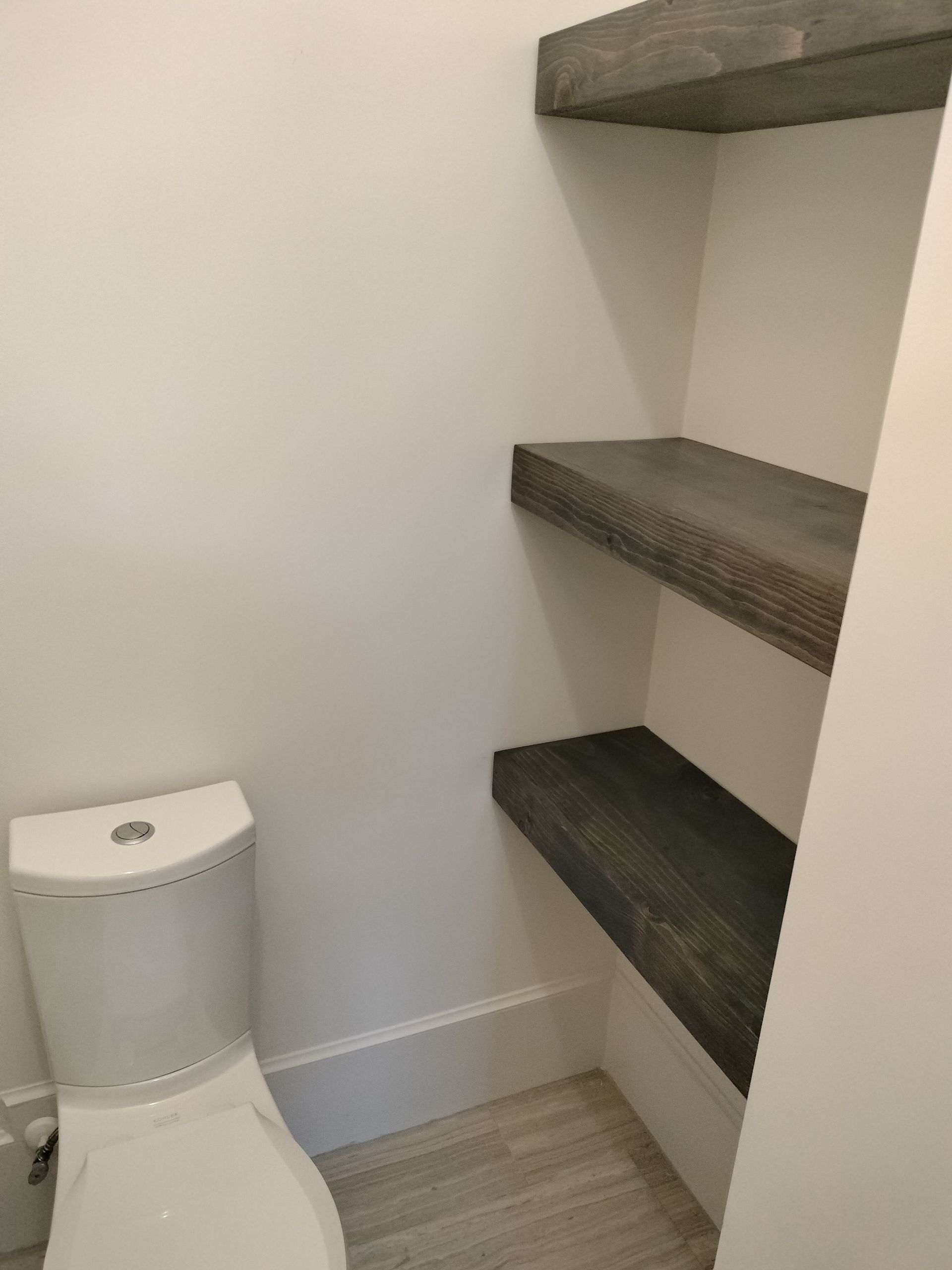 A bathroom with a toilet and shelves on the wall
