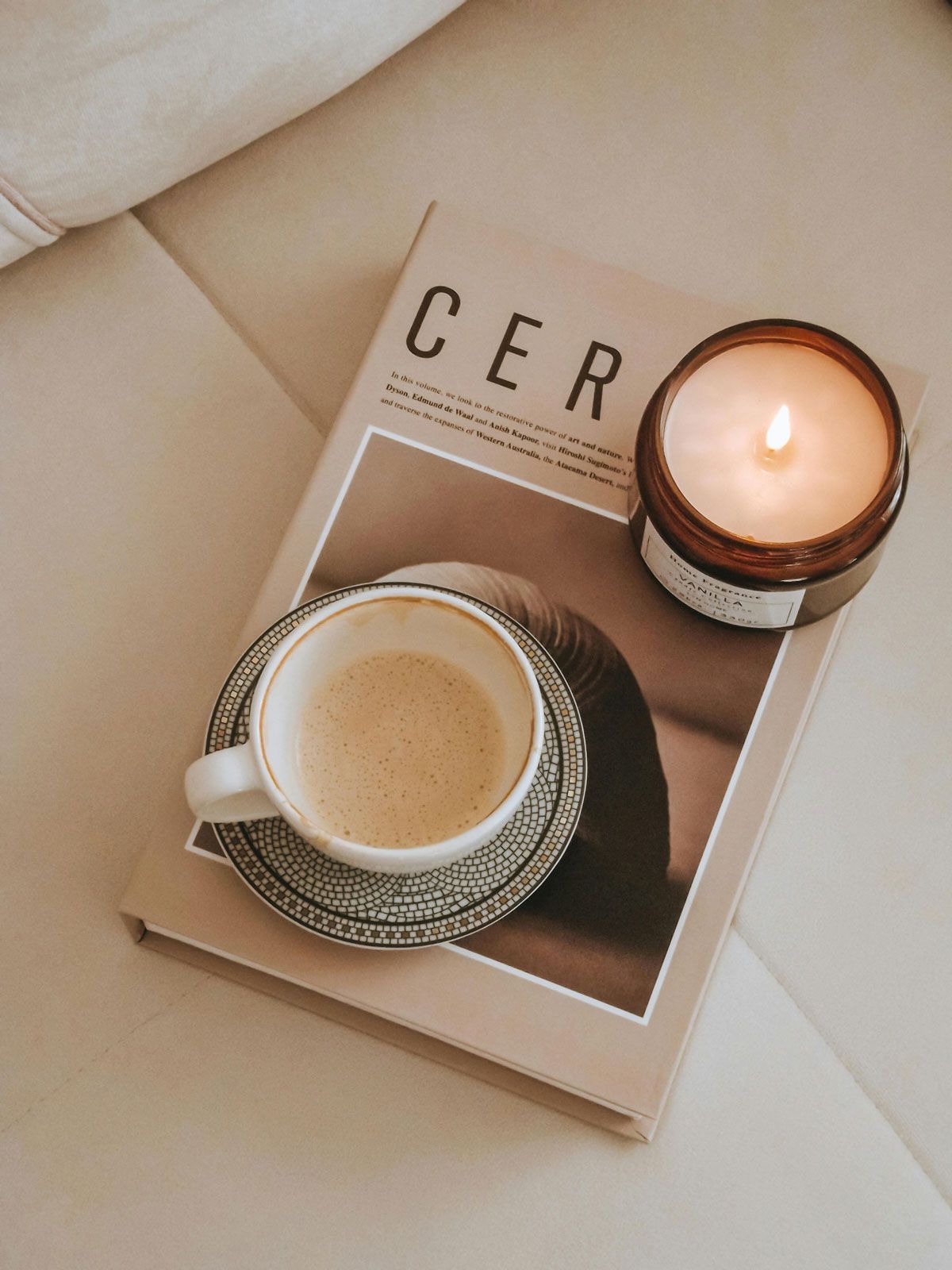 A cup of coffee is sitting on top of a book next to a candle.