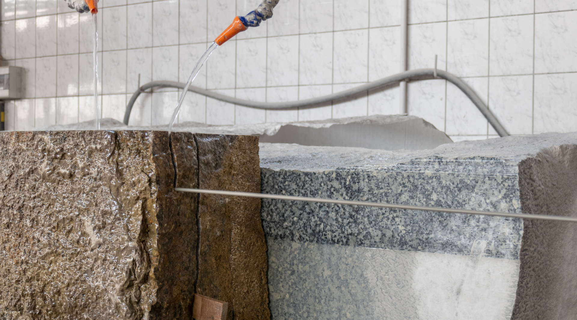 A hose is spraying water on a stone wall.