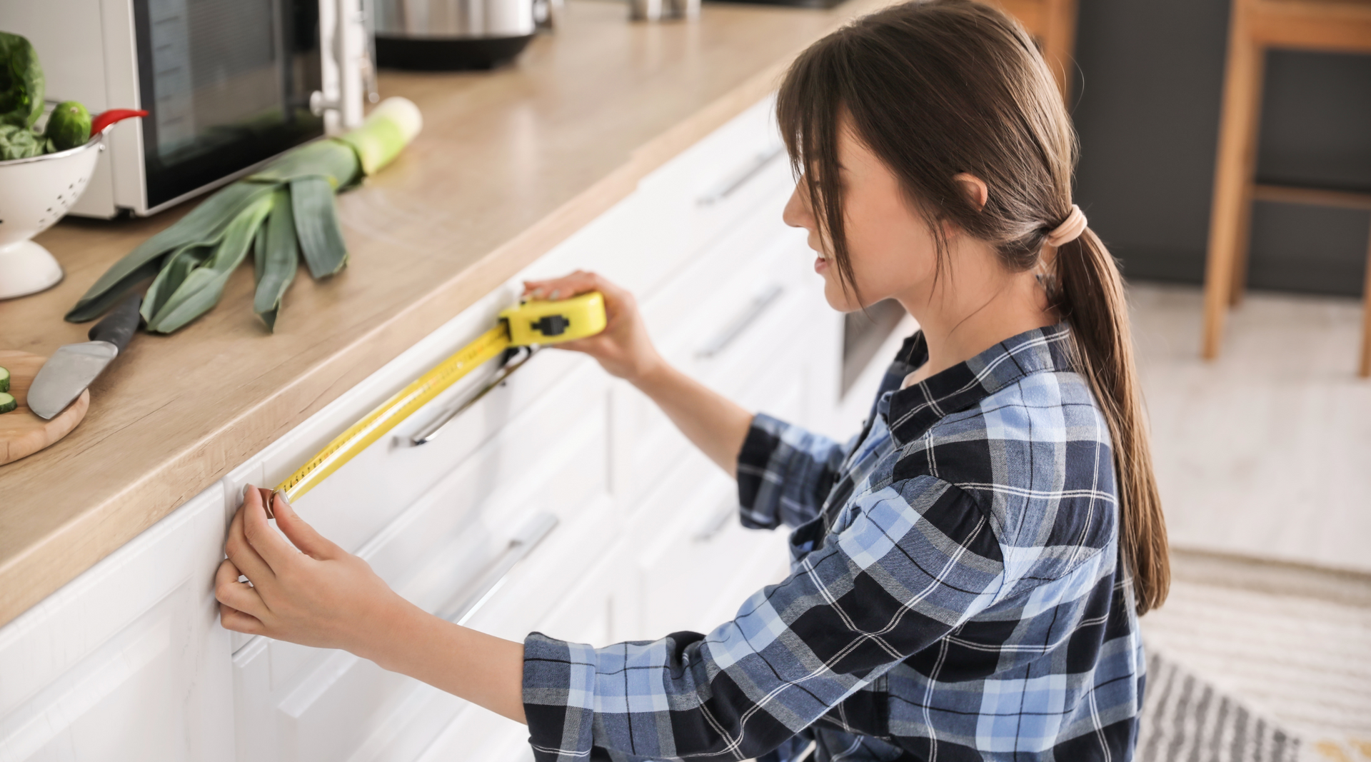 A woman is measuring a kitchen cabinet with a tape measure.
