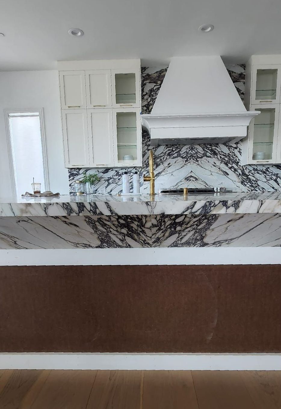 A kitchen with a marble counter top , white cabinets , a stove and a sink.