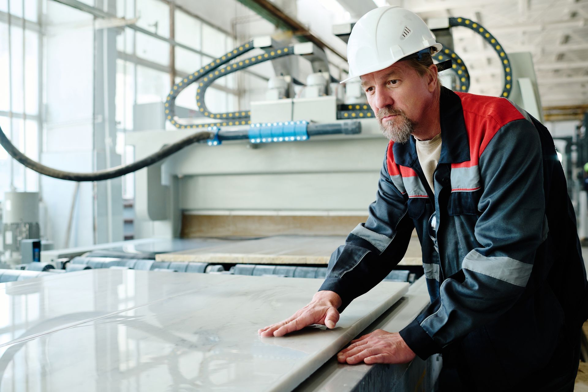A man in a hard hat is standing in front of a machine in a factory.
