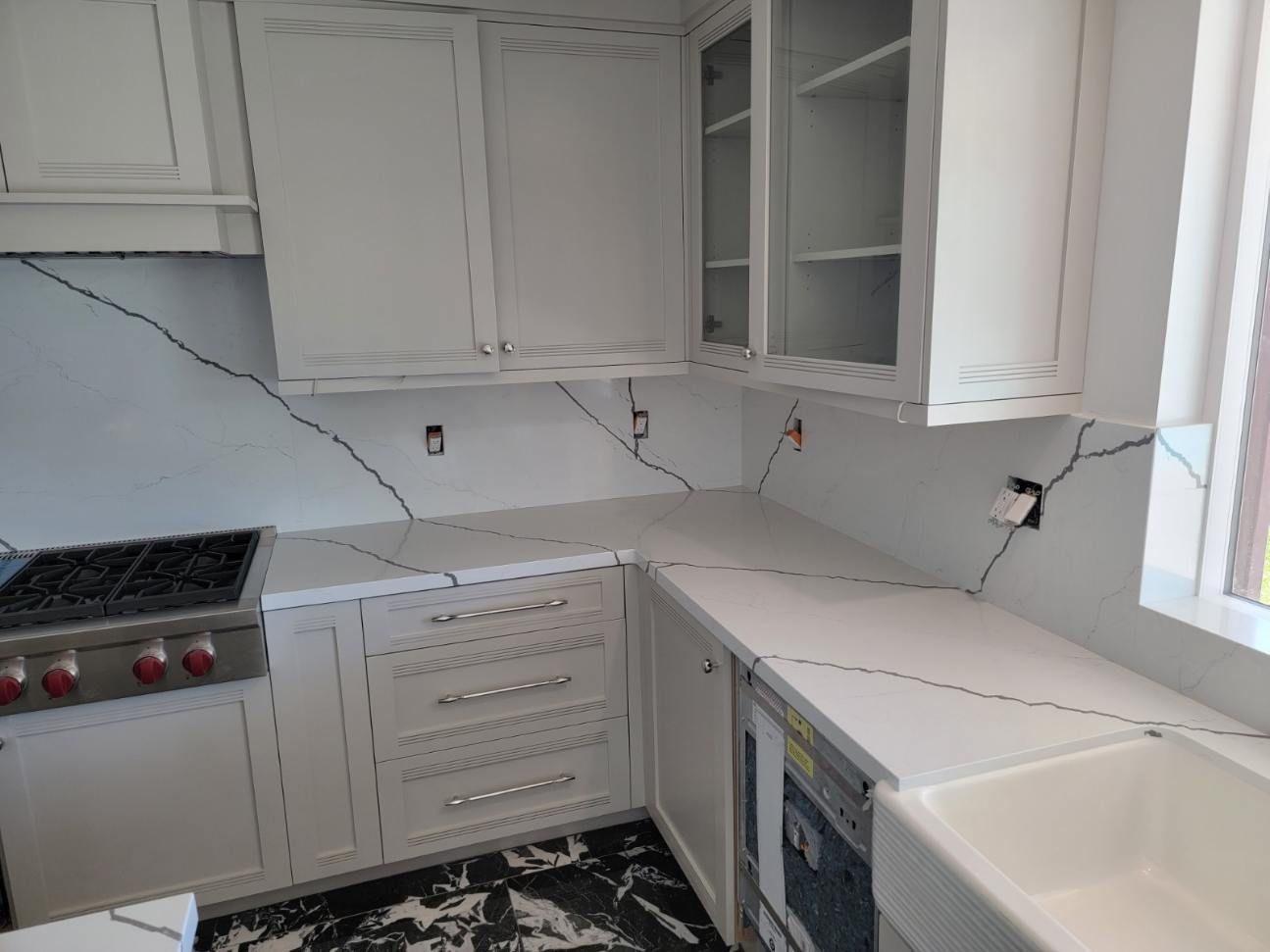 A kitchen with white cabinets , a stove , a sink , and a window.