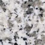 A close up of a white granite counter top with black spots.