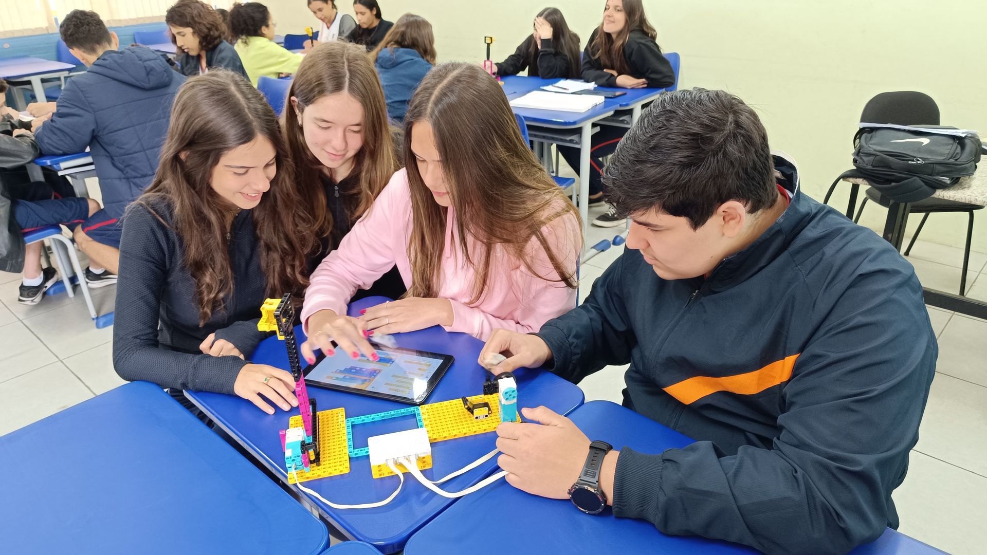 Alunos trabalhando em um projeto de robótica em uma mesa. Um aluno segura um sensor; os outros olham para um tablet.