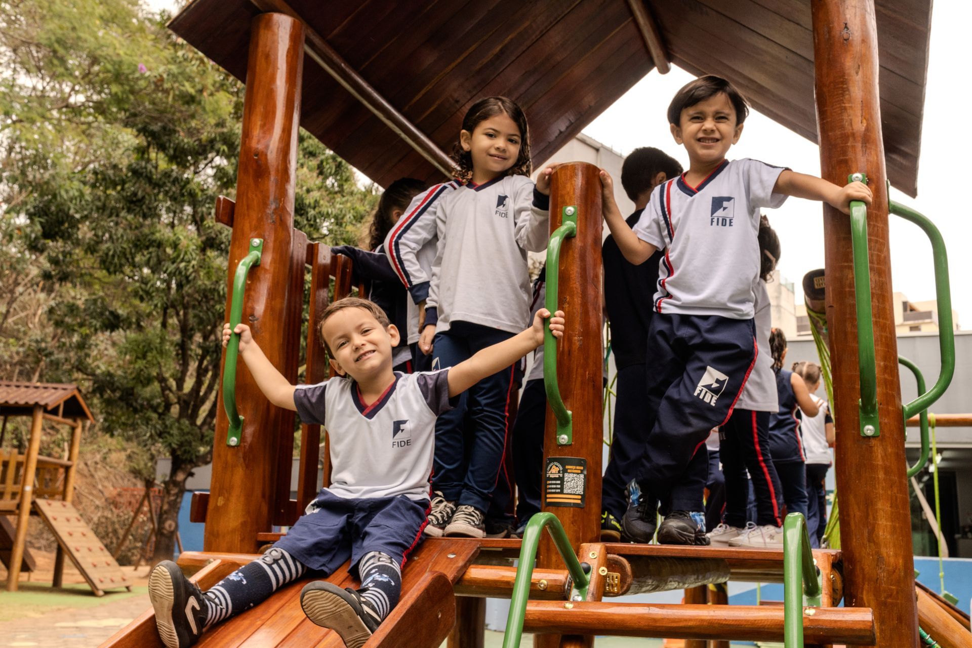 Crianças em uniformes escolares brincando em uma estrutura de madeira para playground.