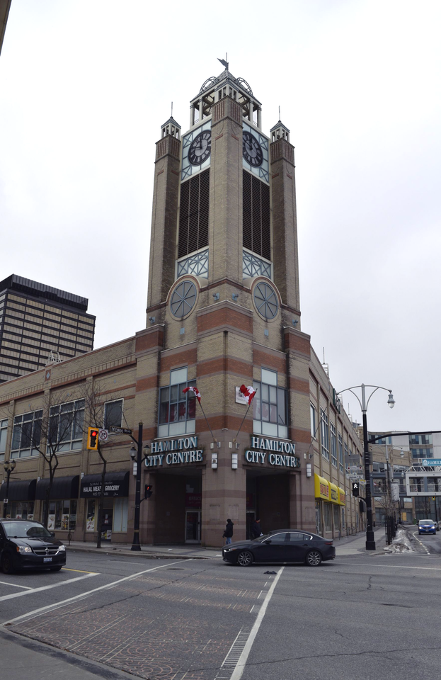 Corner view of a tall ornate brick tower building at a city intersection, with cars and streetlights nearby