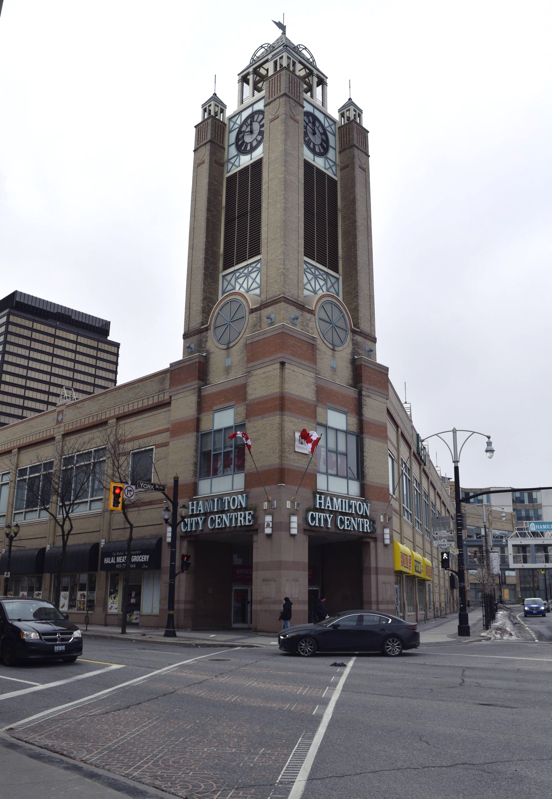 Corner view of a tall ornate brick tower building at a city intersection, with cars and streetlights nearby