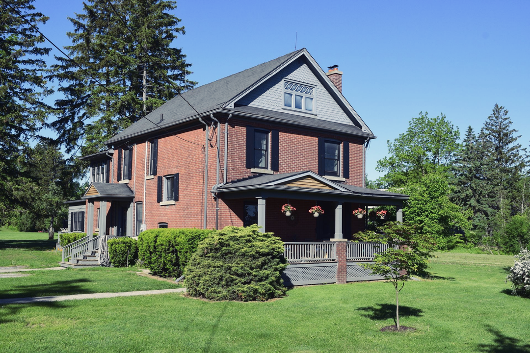Brick house with a covered porch and manicured lawn, surrounded by trees 