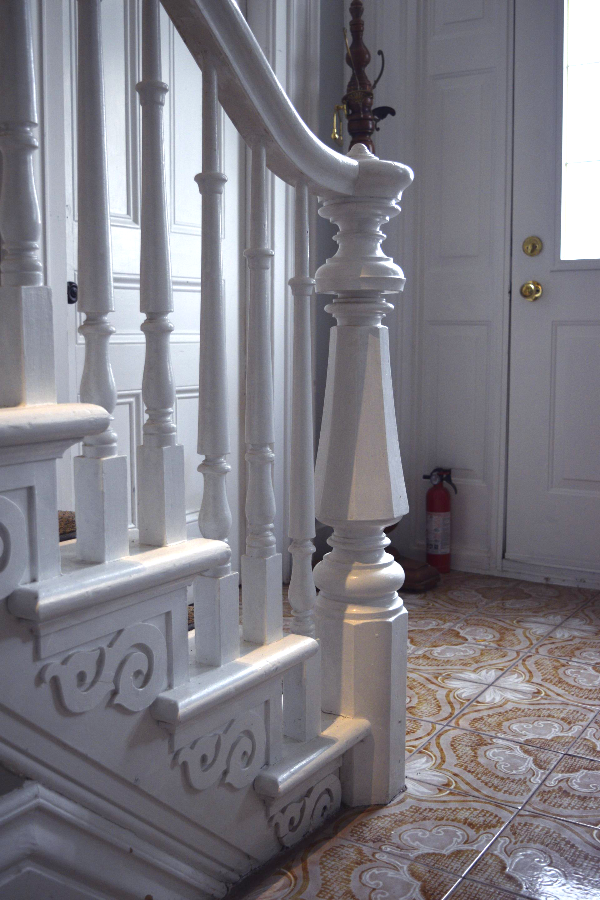 White staircase banister beside a front door in a tiled entryway 