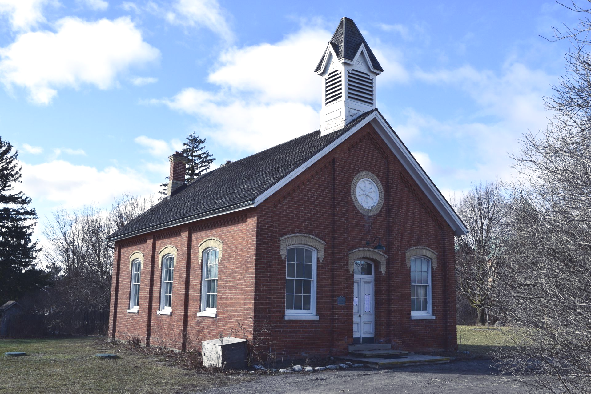 Small red-brick chapel with white trim and a steeple in a grassy field 