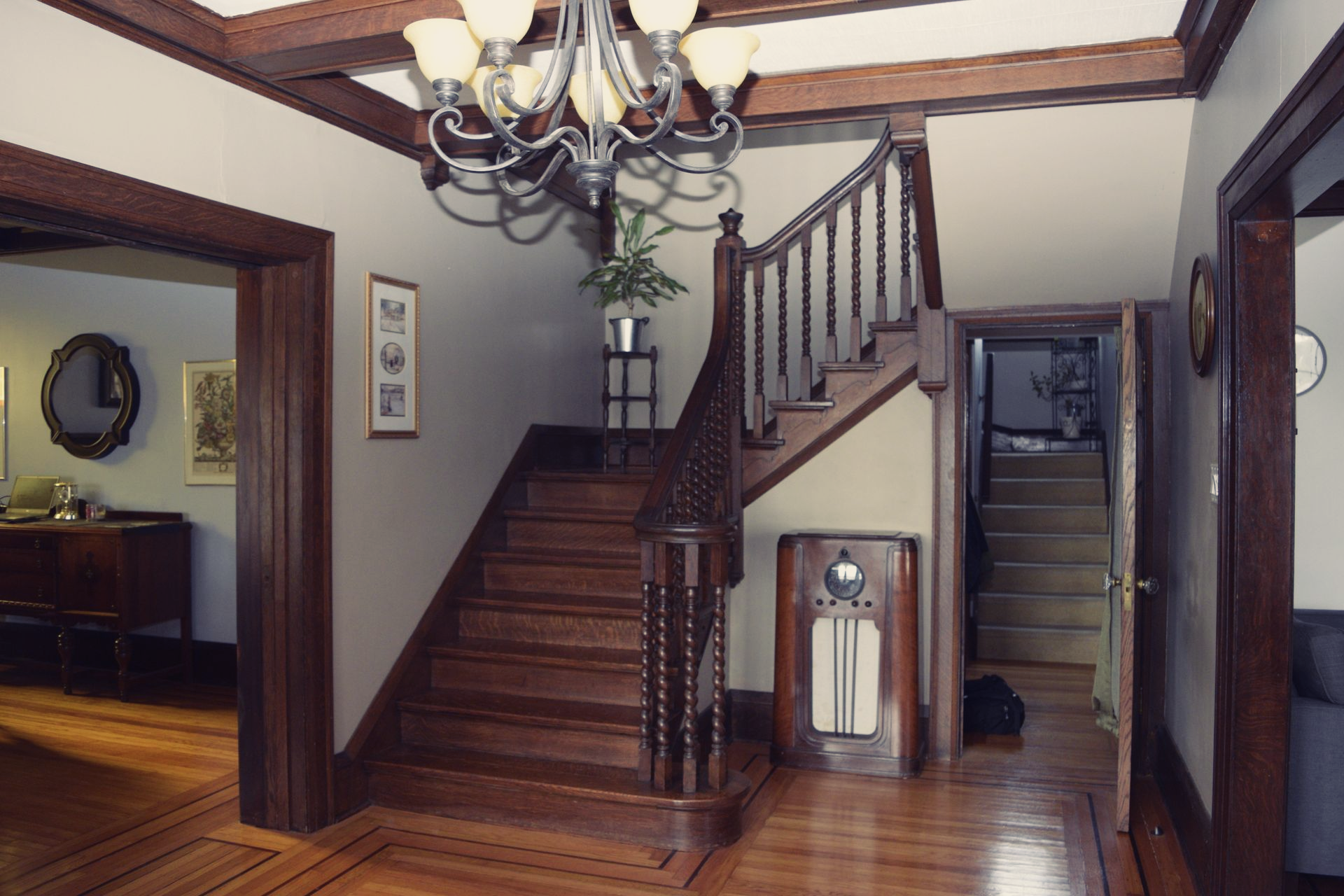 Foyer with wooden staircase, chandelier, and hardwood floors in a vintage-style home