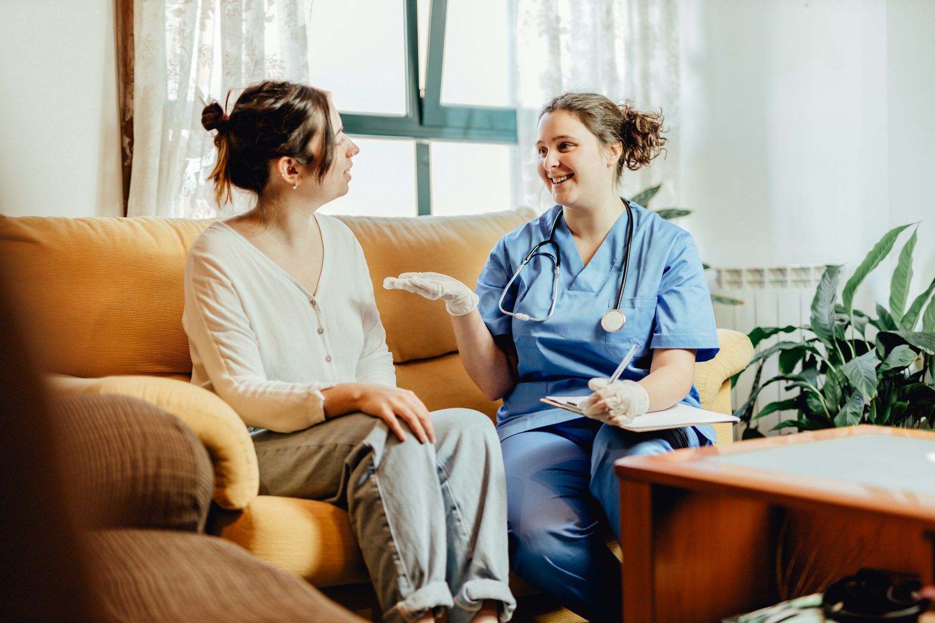 Two women smiling, drinking tea, and eating muffins at a table indoors.