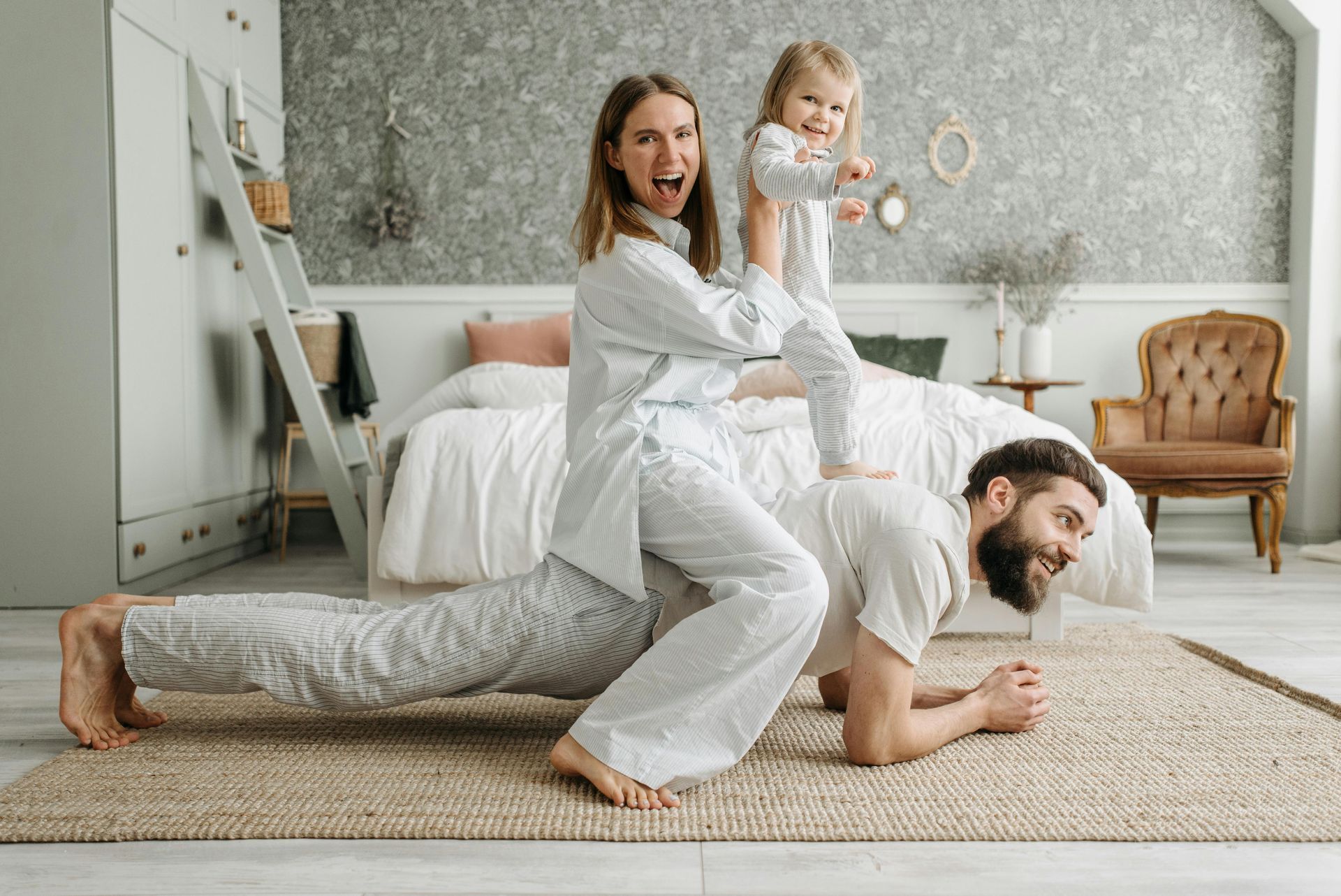 Family playing in bedroom: mother balances on father in plank pose while lifting toddler.