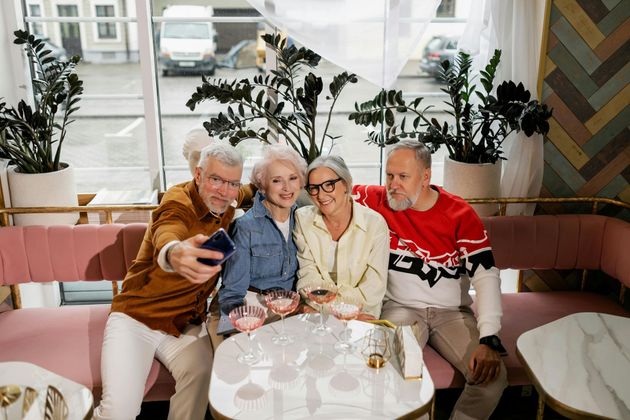 Person in a blazer writing on paper with a silver pen, desk, window in background.