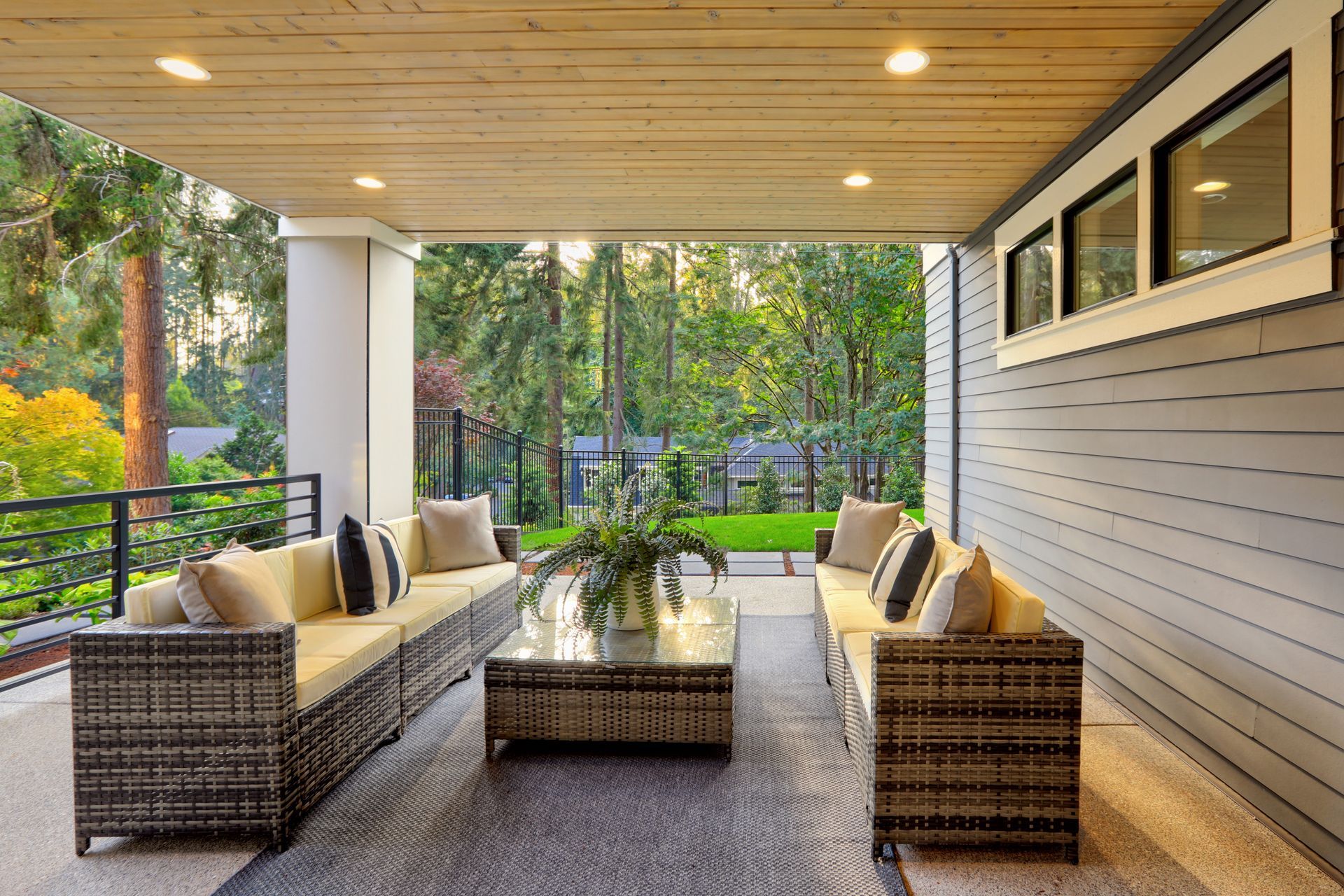Covered patio with wicker seating, coffee table, and wooded garden view at sunset