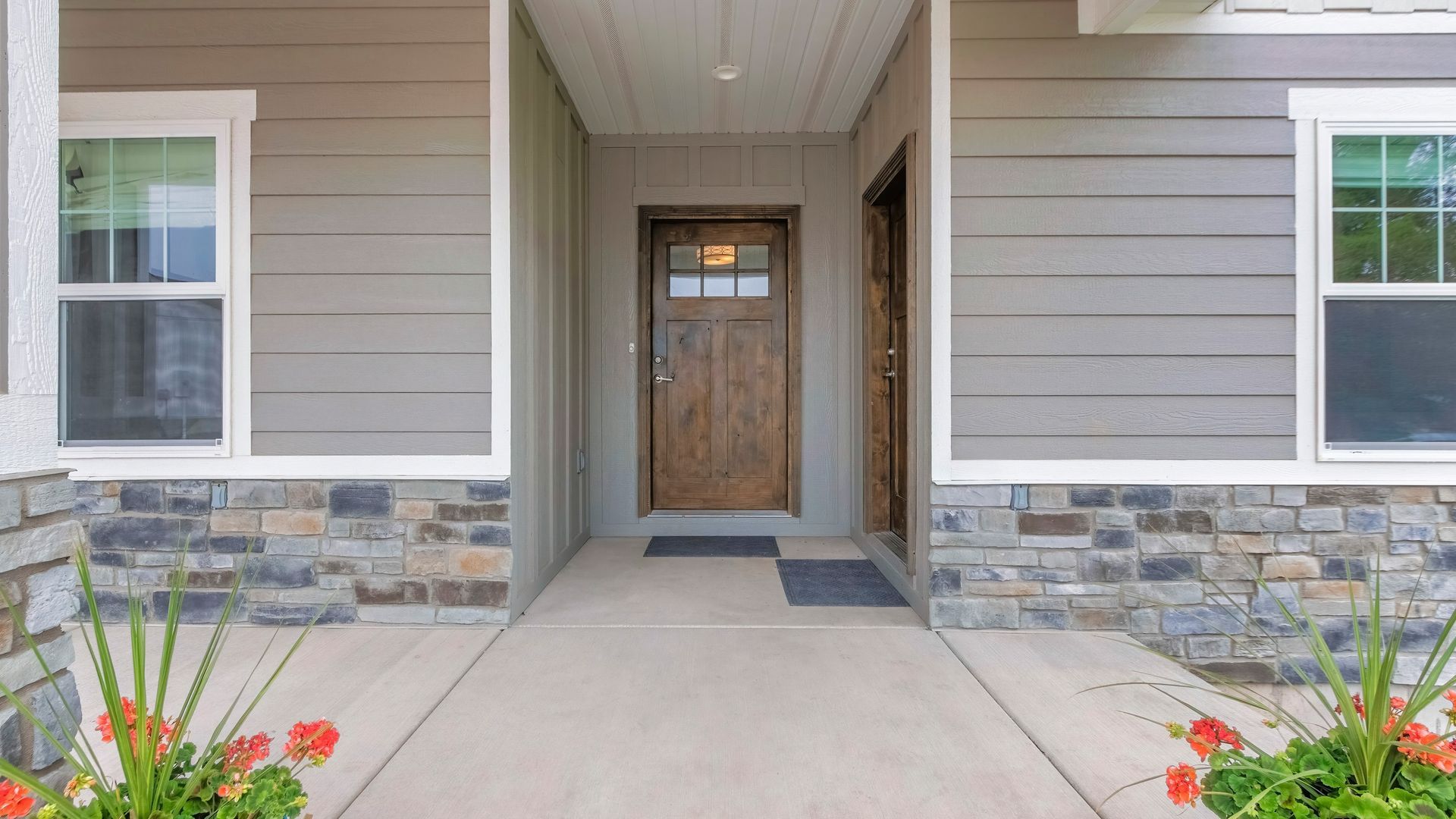 Front porch entrance with stone accents, wood door, gray siding, and flower beds on both sides