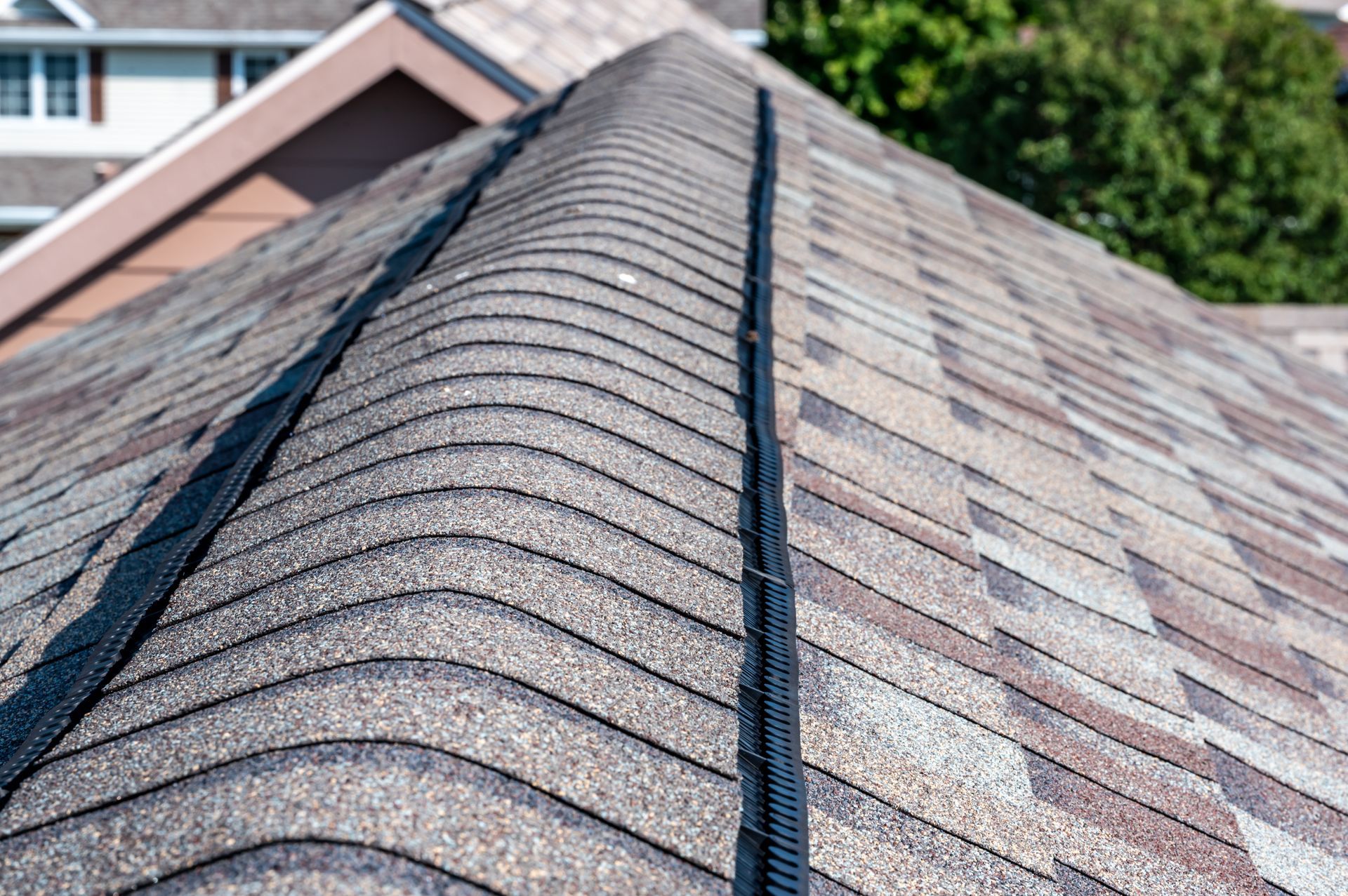 Close-up of a shingled roof ridge with black vent strips, viewed from above