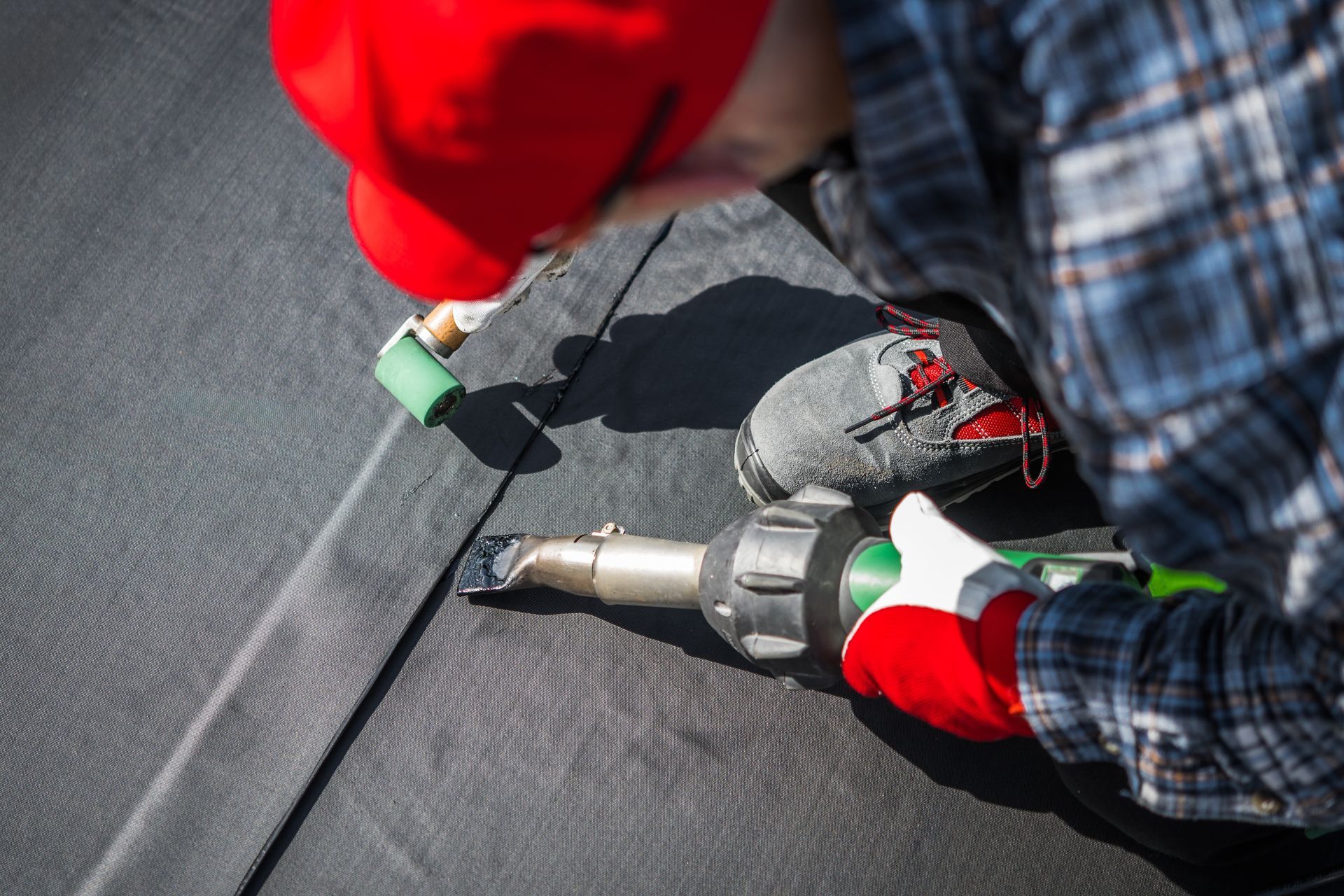 Worker using a nail gun to repair gray roof shingles