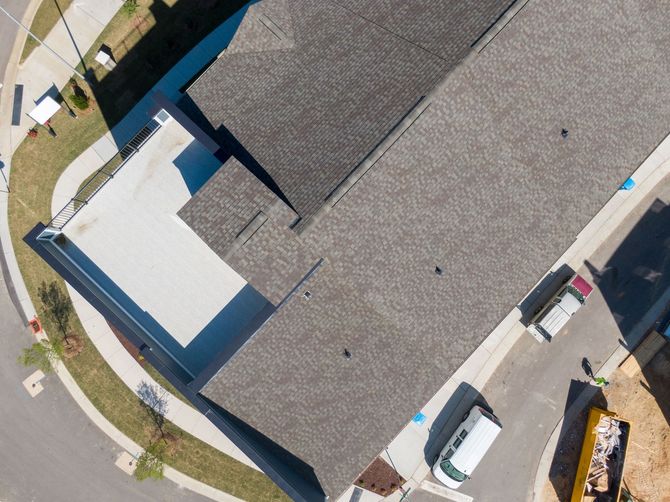 Aerial view of a building with a gray roof beside a street with parked cars and sidewalks