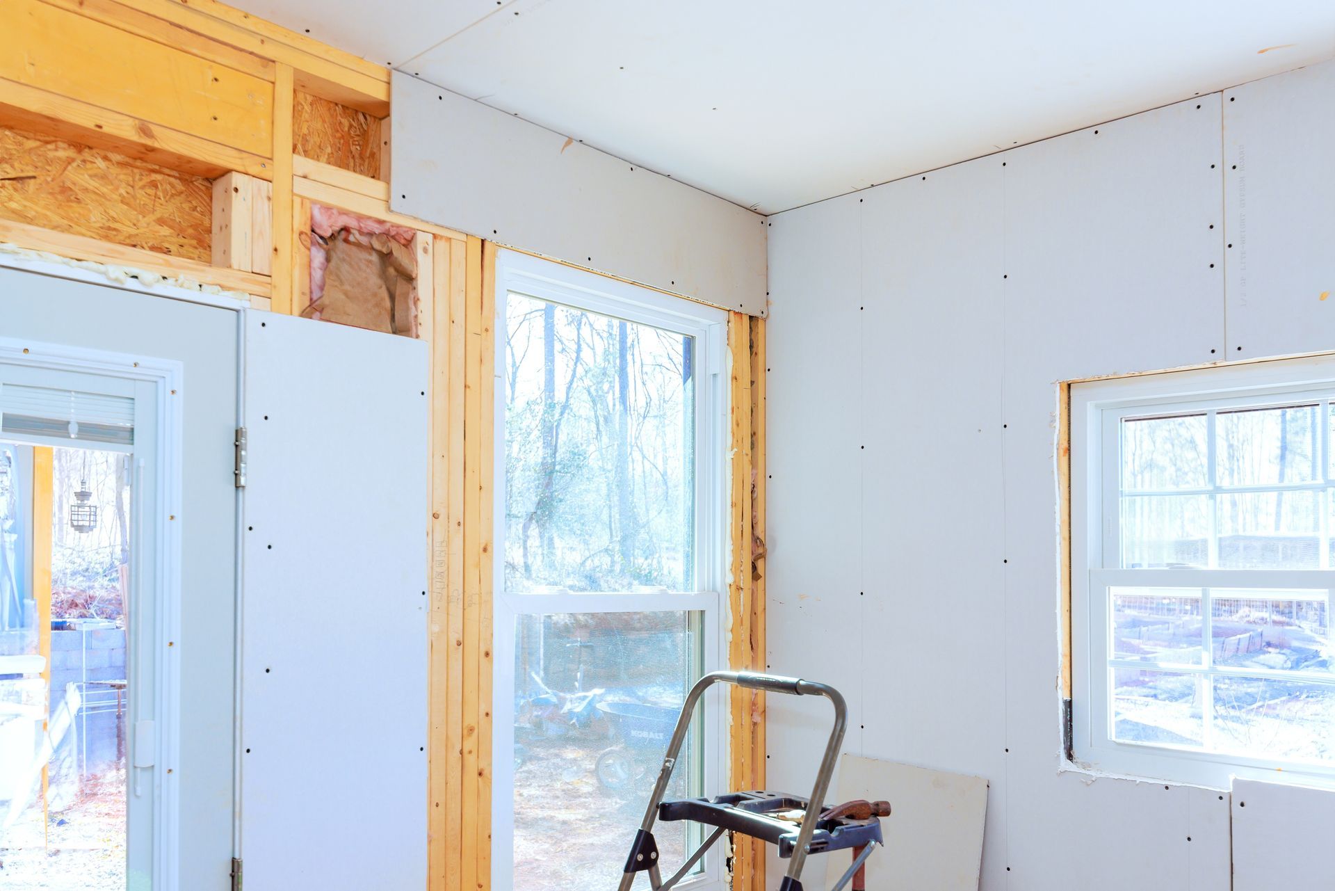 Interior under renovation with exposed framing, windows, and a step ladder near the wall.