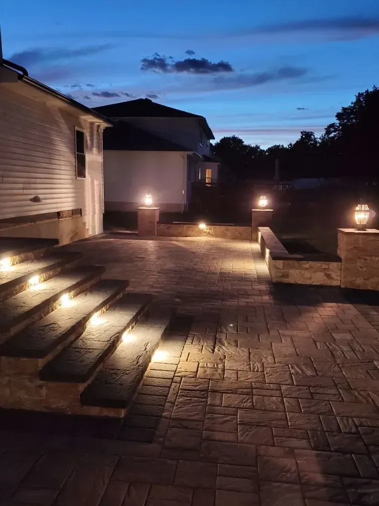 A brick patio with stairs and lights at night.