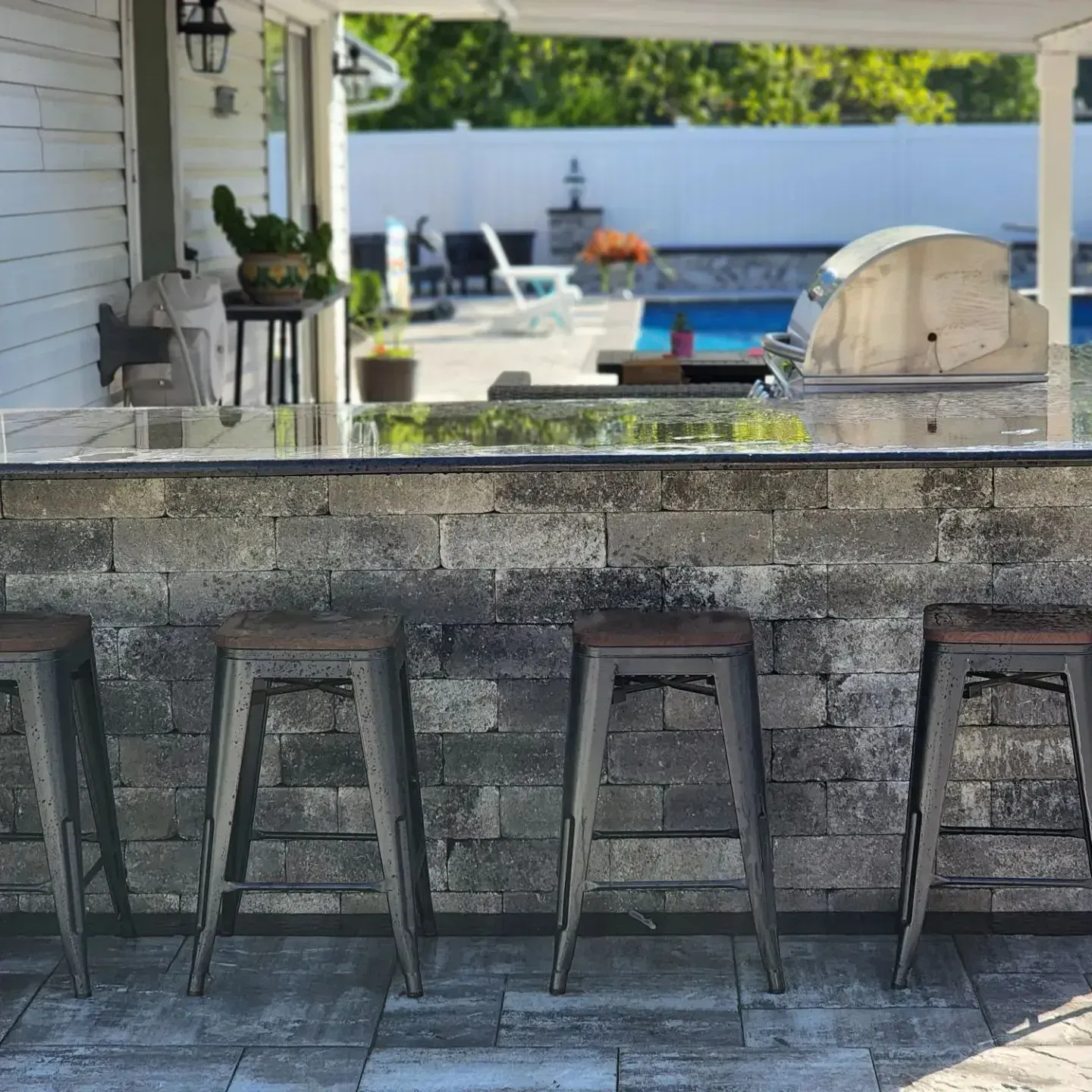 A bar with stools and a grill in front of a pool.