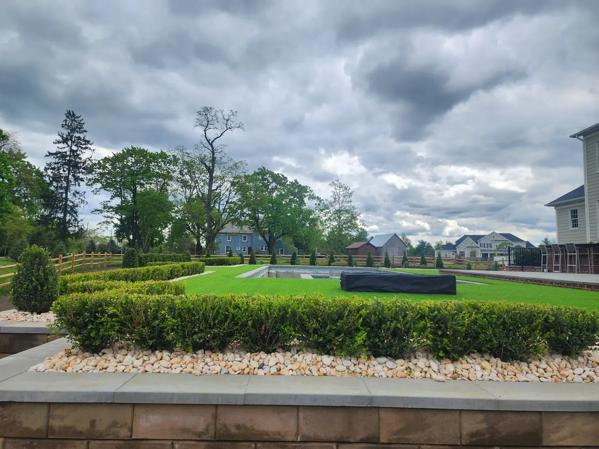 A lush green garden with a brick wall in the foreground and a house in the background.