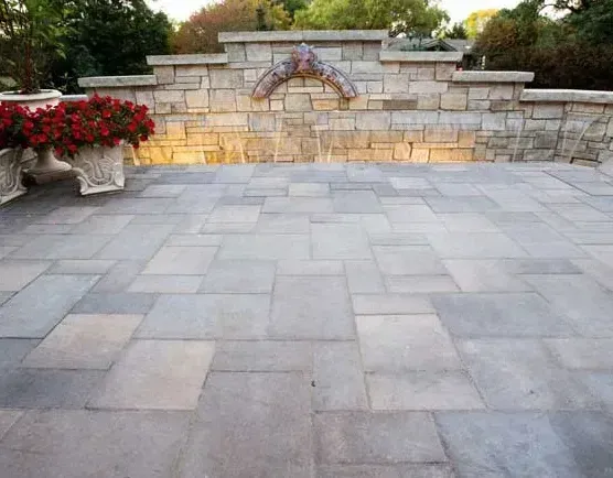 A patio with a stone wall and a fountain in the background.