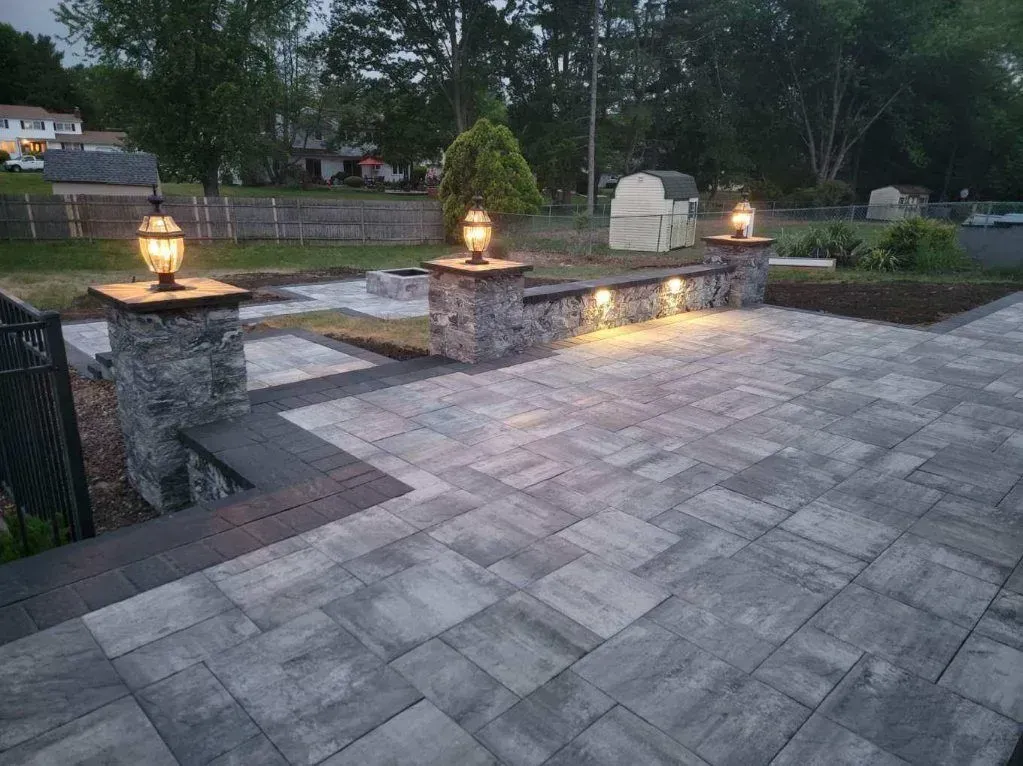 A patio with a stone wall and lights on it at night.