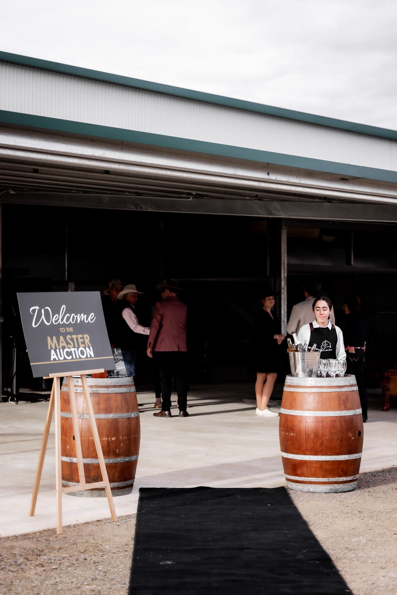 A woman is standing in front of a building with barrels and a sign that says welcome.