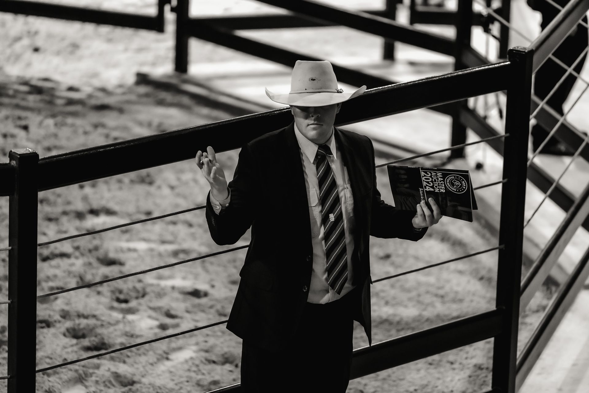 A man in a suit and tie is standing next to a fence holding a book.