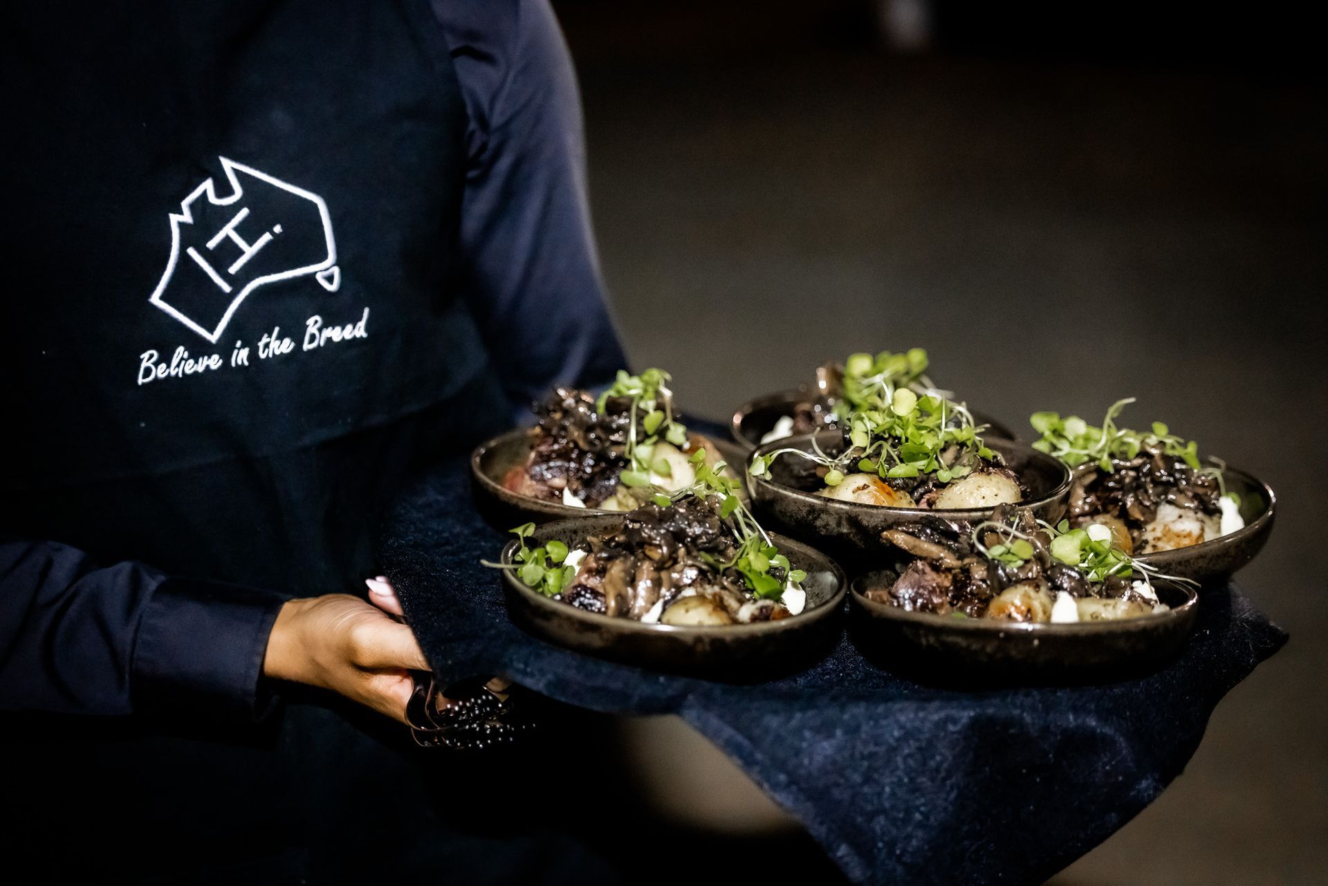 A person wearing a blue apron is holding a tray of food.