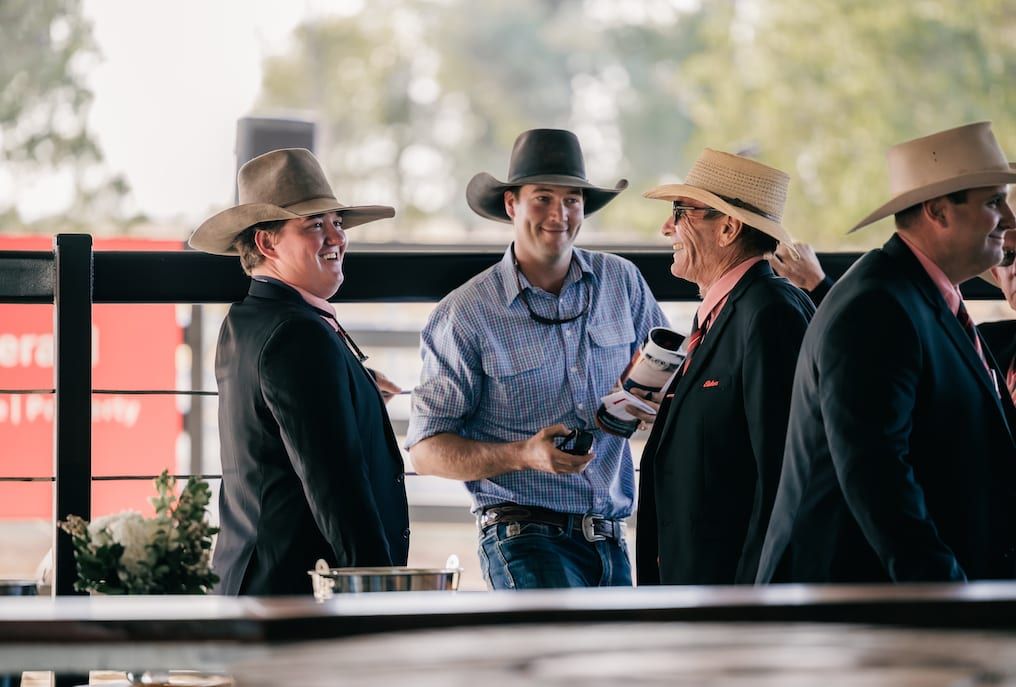 Men in cowboy hats and suits converse outdoors, laughing.