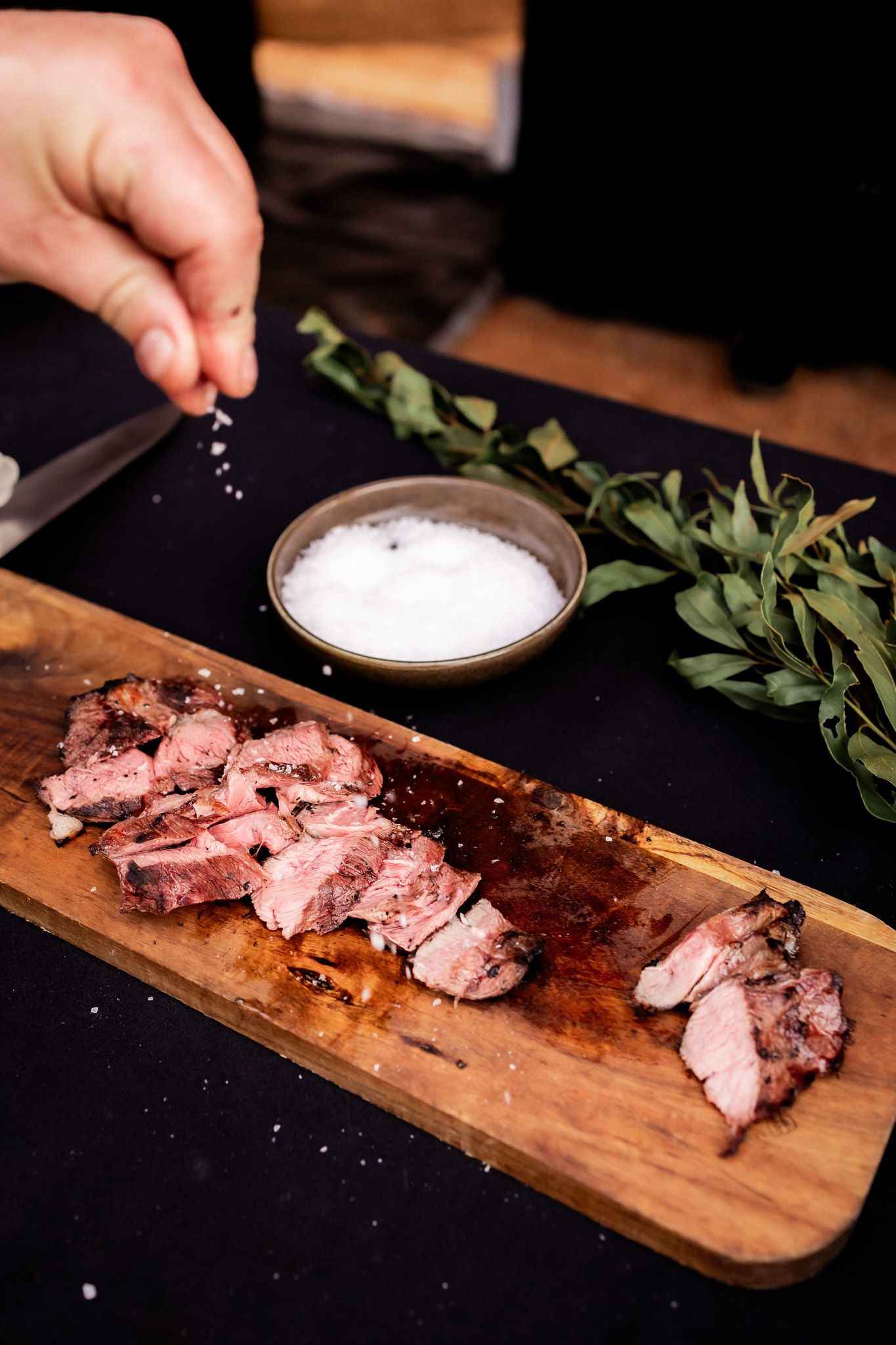 A person is sprinkling salt on a piece of meat on a cutting board.