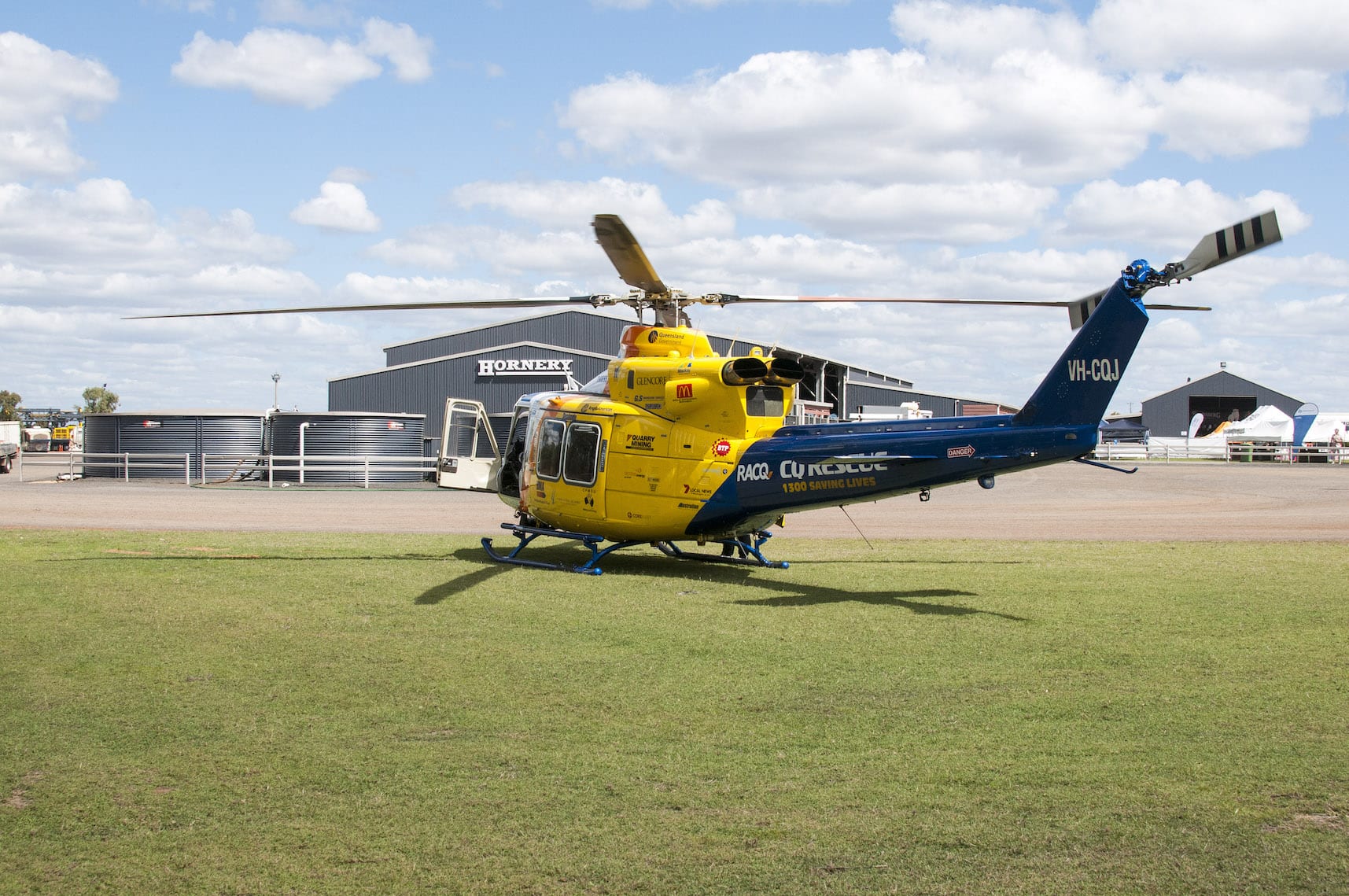 A yellow and blue helicopter is parked on the grass in front of a building.