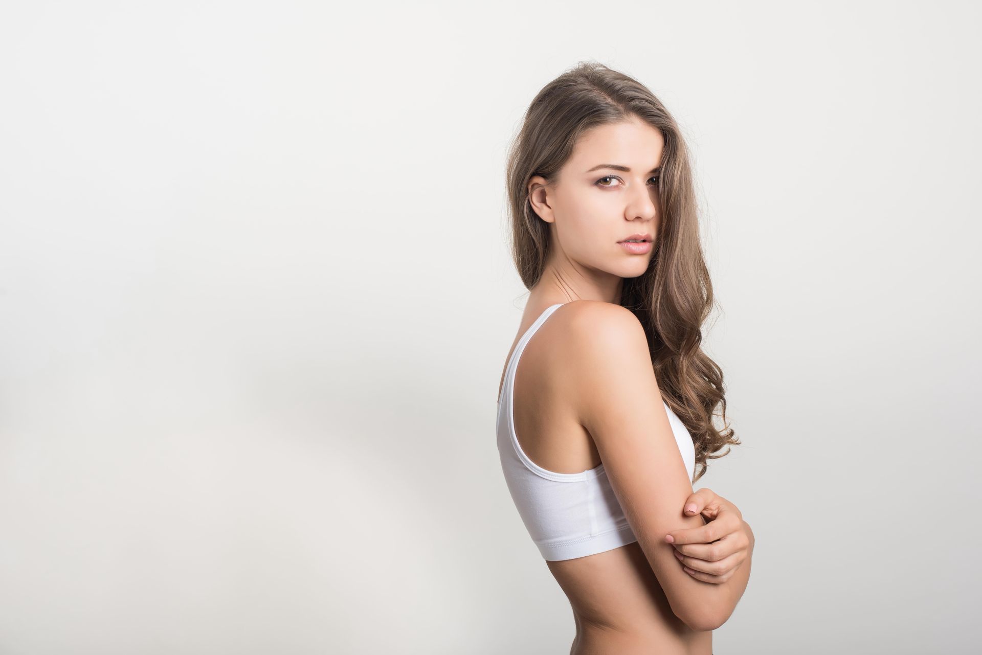 A woman in a white bra is standing with her arms crossed.