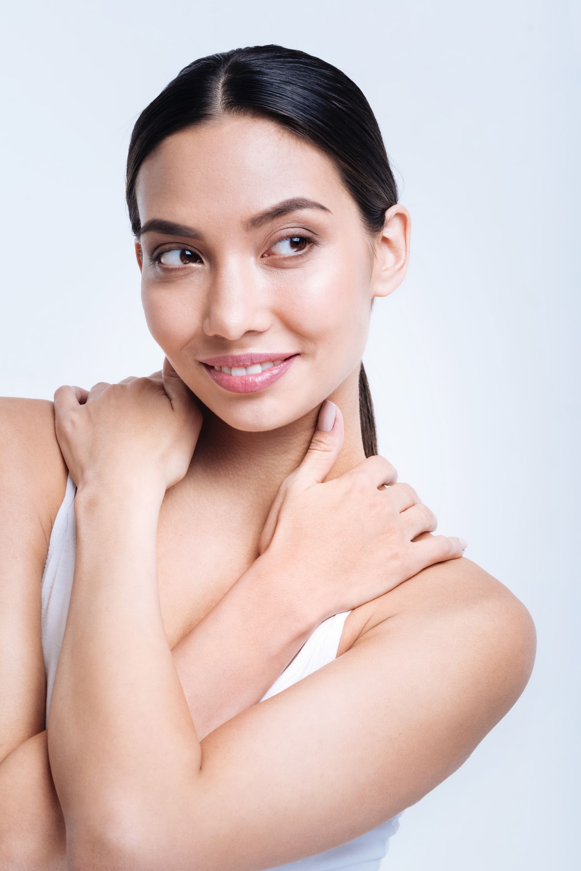A woman is touching her neck with her hands and smiling.