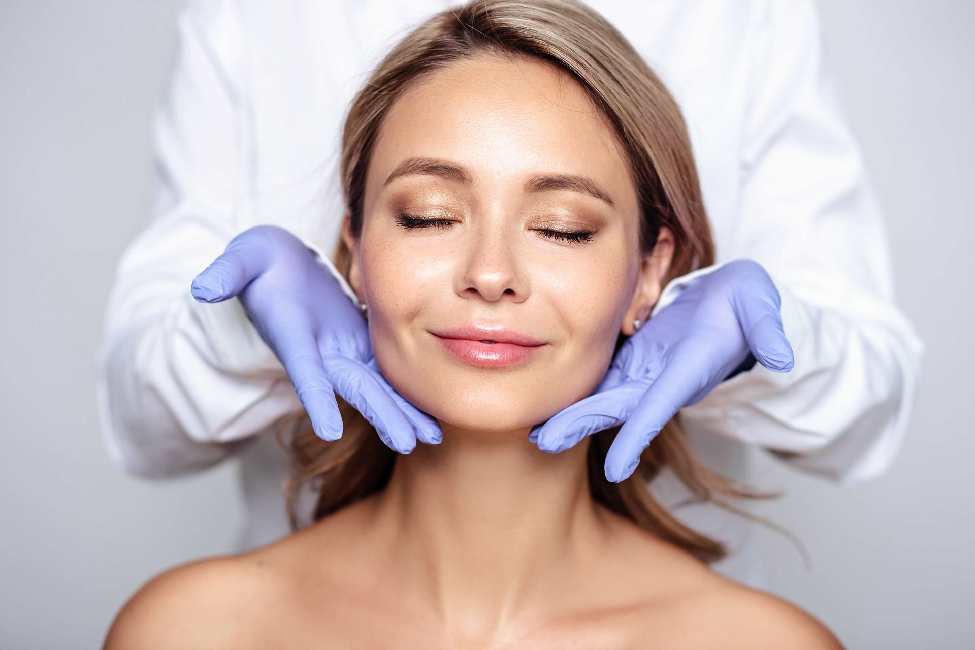 A woman is getting a facial treatment from a doctor wearing gloves.
