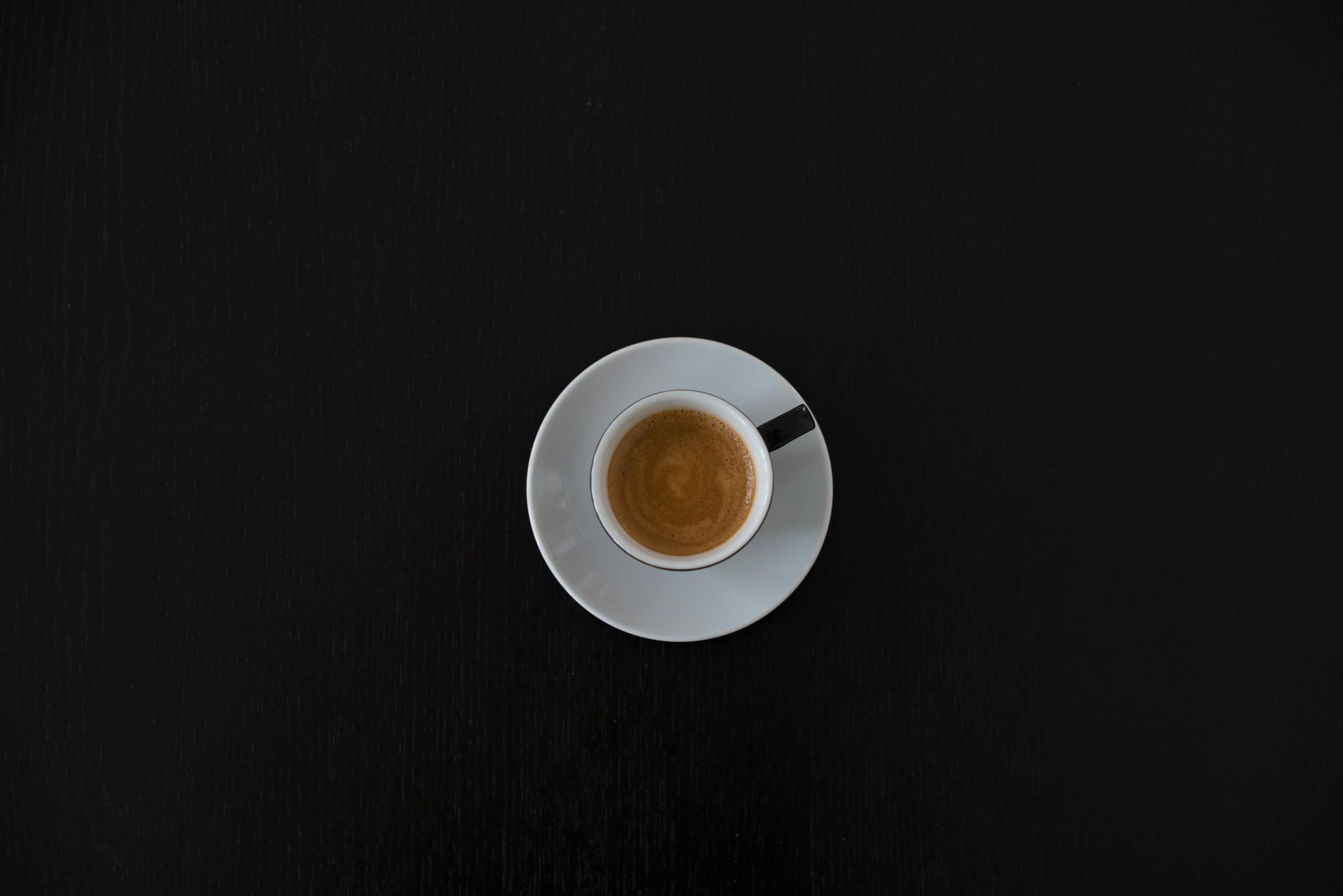 A cup of coffee on a saucer on a black table.