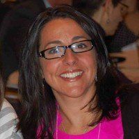 A woman wearing glasses and a pink shirt is smiling for the camera.