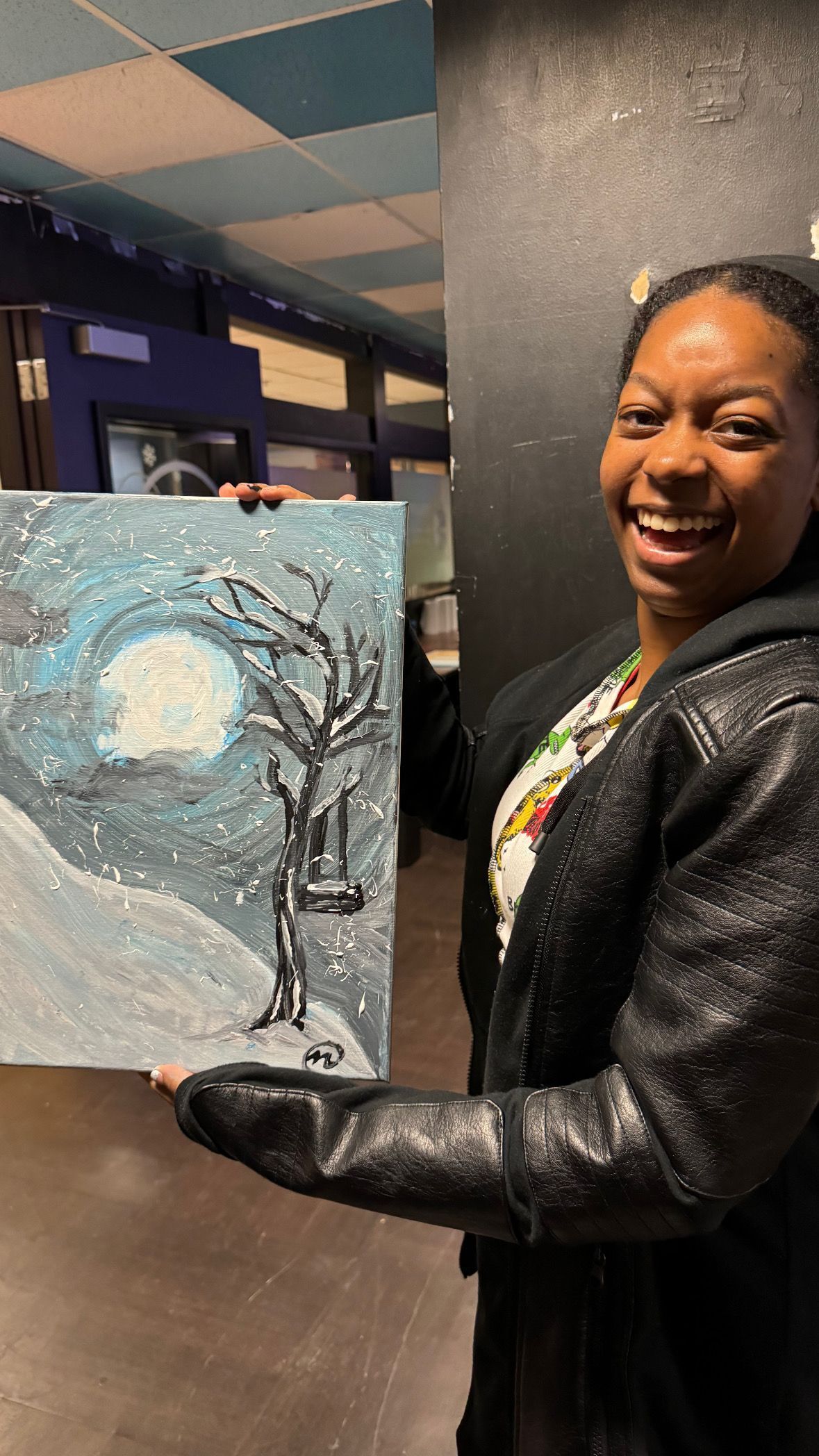 A woman is holding a painting of a tree in the snow.