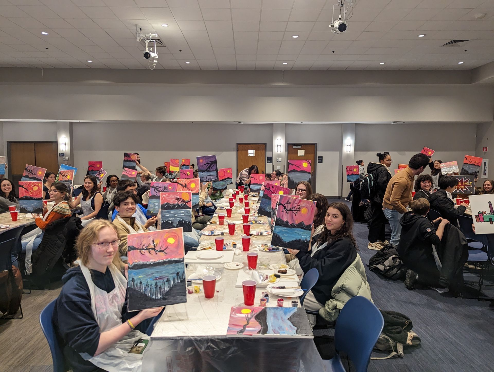 A group of people are sitting at tables in a room with paintings on them.